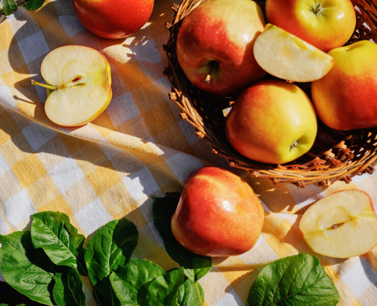 Fresh Red and Yellow Apples in Wicker Basket on Garden Picnic Table