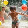 Capture The Fun And Excitement Of Kids Having A Water Balloon Fight In The Backyard, Laughing And Soaking Wet