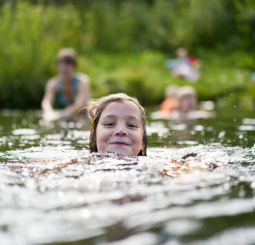 The Girl Swims Against The Background Of Bathing Other Family Members.