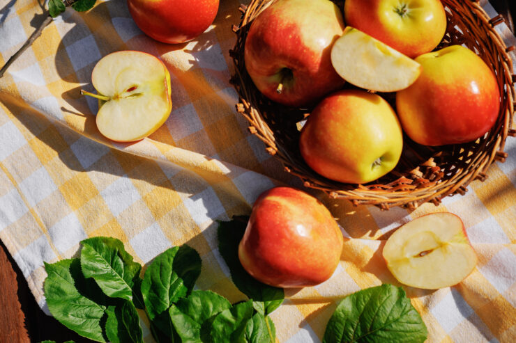 Fresh Red and Yellow Apples in Wicker Basket on Garden Picnic Table